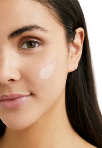 Light moisturizer applied to the cheek, creamy texture, slightly translucent with a subtle shine. Smooth skin with natural color tones.
