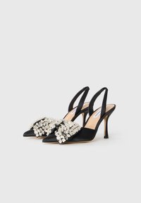 Le décolleté in satin nero presenta una punta affusolata e un'decorazione di gemme sulla parte frontale. Il tacco è slanciato e misura circa 10 cm.