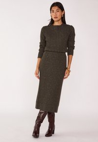 Ensemble robe deux pièces tricoté avec une texture côtelée en vert foncé aux fils argentés, col rond, silhouette ajustée, associé à de grandes bottes bordeaux.