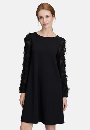 Schwarzes Kleid mit rundem Ausschnitt und langen, transparenten Ärmeln, verziert mit schwarzen Federdetails. Glatter Stoff und ausgestellte Silhouette.