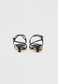 Czarne sandały na obcasie typu kitten heel z cienkimi paskami wokół kostki ozdobionymi małymi cyrkoniami, pokazane od tyłu na białym tle.