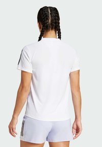 Camiseta deportiva blanca con una tela texturada, mangas cortas y rayas negras contrastantes en los hombros. Modelo de espaldas a la cámara.