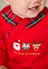 Rød heldragt med et ternet kravesnit, prydet med broderede nisser, juleskinke og rensdyr, samt teksten "min første jul."