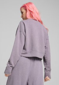 Sudadera recortada de tejido morado claro. Presenta puños anchos y un cuello redondo, con una textura suave y un corte relajado.