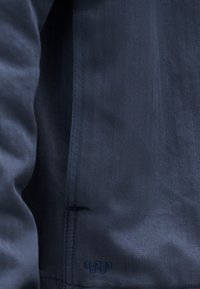 Κοντινό πλάνο ύφανσης ψαροκόκκαλου σε ναυτικό μπλε, με ραμμένη ραφή και μικρό μοτίβο καρό κοντά στο κάτω άκρο.