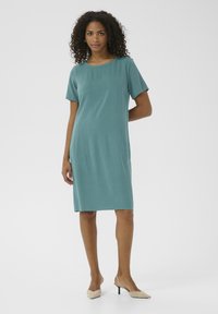 Türkises Kurzarmkleid mit runder Ausschnitt, geradem Schnitt und seitlichen Taschen, gefertigt aus einem glatten, leichten Stoff.