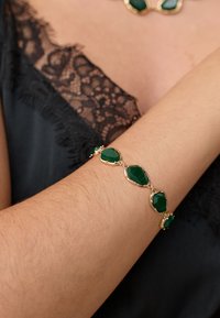 Gold-tone bracelet featuring green faceted stones in an oval shape, set in a delicate linked design, worn on a bare arm.
