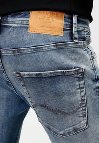 Detailní záběr zadního kapsy modrých džínů z denimu s hnědou koženou značkou Jack & Jones nad kapsou.