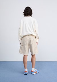 Beige cargoshorts med flera fickor, i kombination med en löst sittande krämfärgad topp. Blå och orange sneakers fulländar outfiten.