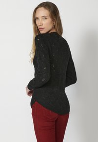 Czarny sweter z dzianiny o fakturowanym wzorze, z długimi rękawami i zaokrąglonym dołem, zestawiony z czerwonymi spodniami w wąskim fasonie.