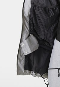 Lehká bunda s šedým a černým vnějším povrchem. Vnitřek má texturovanou černou podšívku a detaily se zacvakáváním. Šňůrka na lemu.