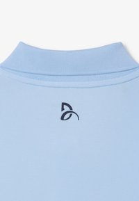 Polo-shirt bleu clair en tissu texturé, avec un logo foncé au niveau de l'encolure arrière. Le col est côtelé et structuré.