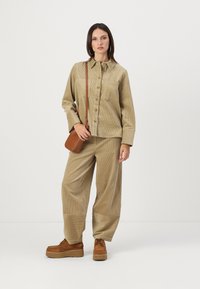 Beige cordfløyels skjorte, løse bukser og brune platå sko. Detaljer inkluderer knapper, lomme og en liten brun crossbody-veske.