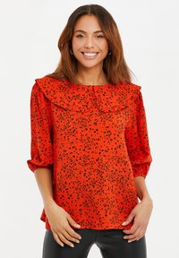 Rode top met zwart luipaardprint, voorzien van een gerimpelde kraag en driekwartmouwen. Gemaakt van een lichte stof met een losse pasvorm.