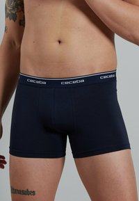 Navy blue boxer briefs made of soft fabric, featuring a white waistband with “ceceba” logo and a snug fit, with a smooth texture.