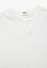 Camiseta de algodón blanca con cuello redondo, tapeta de tres botones y mangas cortas. Textura suave, diseño minimalista y sin patrones.