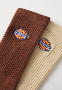 Calzini di cotone ribstop marroni e beige con logo "Dickies" intrecciato in accenti rossi, gialli e blu. La texture del tessuto è morbida e flessibile.