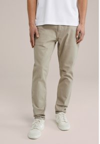 Beige katoenen slim-fit broek met een gladde textuur, voorzien van voorzakken en een ritssluiting, gecombineerd met witte sneakers.