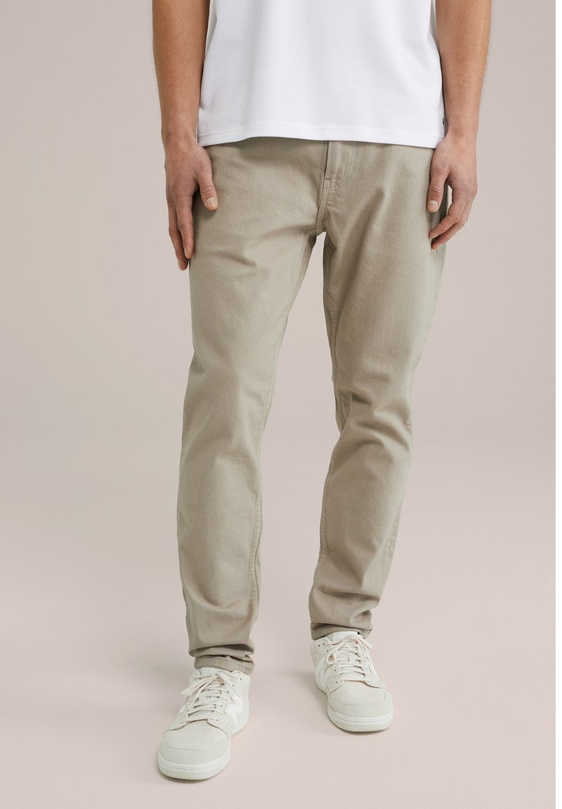 Beige katoenen slim-fit broek met een gladde textuur, voorzien van voorzakken en een ritssluiting, gecombineerd met witte sneakers.