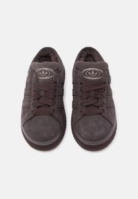 Καφέ σουέτ αθλητικά παπούτσια με υφή στο σχεδιασμό, στρογγυλή μύτη, χοντρές κορδόνια και λαστιχένια σόλα· διαθέτουν έναν κυκλικό λογότυπο στη γλώσσα.