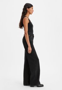 Črne široke hlače iz jeansa z visokim pasom, z teksturiranim zaključkom in minimalnim šivanjem. Kombinirane z oprijetim črnim topom brez rokavov.