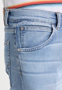 Ljusblå jeans i klassisk passform med en krökt ficka, kontrasterande sömmar och en jämn textur.