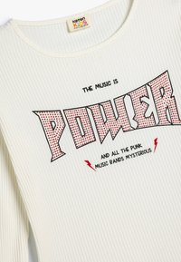 Hvid ribbet langærmet skjorte med rød trykt tekst, der siger "POWER," med sorte konturer og lynaccentueringer.