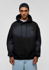 Zwarte gradient hoodie met een voorzak, trekkoorden en een logo op de borst. Gemaakt van zachte stof met een relaxte pasvorm.