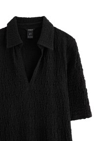 Robe noire à texture avec un col en V, des manches courtes et un décolleté plongeant. Fabriquée à partir d'un tissu froissé pour plus de dimension.