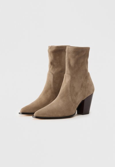 Tan suede ankle boots with a pointed toe, featuring a stacked wooden heel and seamless design. Soft texture with no visible hardware.