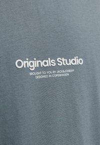 T-shirt en coton gris arborant le texte de marque blanc "Originals Studio" et "présenté par JACK & JONES, conçu à Copenhague."