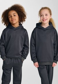 Två barn har på sig matchande mörkgrå huvtröjor och byxor. Tyget verkar slätt med en subtil lyster; har ribbade ärmslut och midjeresår.