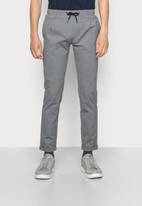 Grå tapered bukser lavet af blødt stof, med en drawstring talje, sidelommer og optrukne manchetter, parret med grå sneakers.