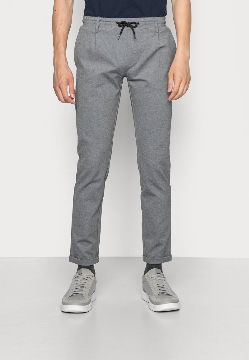 Grå tapered bukser lavet af blødt stof, med en drawstring talje, sidelommer og optrukne manchetter, parret med grå sneakers.