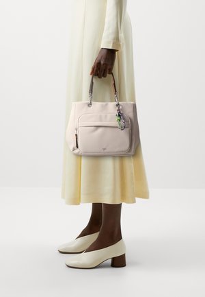 Sac à main synthétique rose clair avec une poche avant et un porte-clés coloré, associé à une robe pastel jaune fluide et des chaussures à talons off-white.