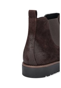 Brązowy zamszowy botek za kostkę z elastycznym panelem bocznym, teksturowanym wykończeniem i czarną gumową podeszwą. Zauważalne detale przeszycia wzdłuż krawędzi.