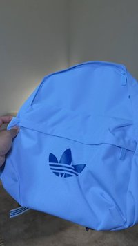 Světle modrý batoh z odolné látky s vyřezávaným logem se třemi pruhy. Na vrchu je kapsa na zip a nastavitelné ramenní popruhy.