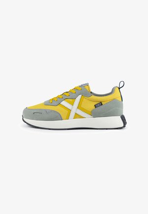 Zapatillas deportivas en amarillo y gris con parte superior de tela, suela de goma y acentos en blanco. Presentan un diseño con cordones y una pestaña de tirón en la parte trasera.