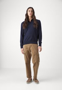 Μπλε μακρυμάνικη πουκάμισο πόλο με ριγωτό στρίφωμα, συνδυασμένο με καφέ cargo παντελόνι με πλαϊνές τσέπες και χαλαρή εφαρμογή. Καφέ παπούτσια slip-on.