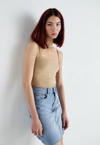 Beige fitted tank top with spaghetti straps paired with a light blue denim skirt featuring a curved hem and front pocket.