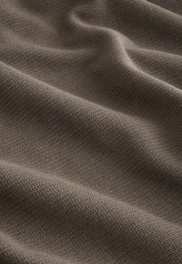 Primer plano de una suave tela de punto color topo con un fino patrón texturizado y pliegues suaves que crean luz y sombra.