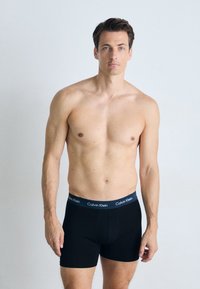 Zwarte katoenen boxershorts met een aansluitend ontwerp en het Calvin Klein-logo op een elastische tailleband, gedragen door een mannelijk model in een neutrale setting.