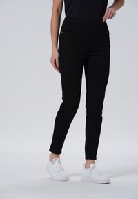 Zwarte stretch broek tot de enkels met een elastische tailleband, met een slim fit en zijzakken, gecombineerd met witte sneakers.