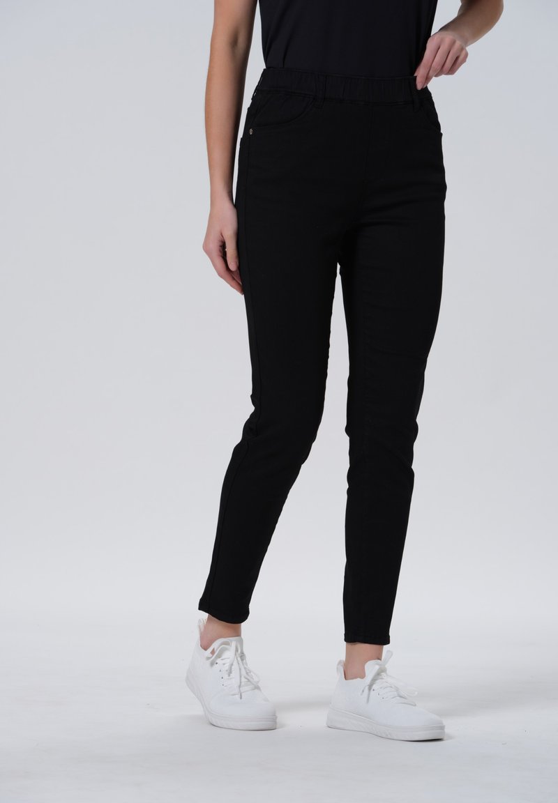 Zwarte stretch broek tot de enkels met een elastische tailleband, met een slim fit en zijzakken, gecombineerd met witte sneakers.