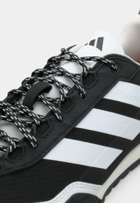 Μαύρο αθλητικό παπούτσι με λευκό σχέδιο τριών ριγών, υφαντό ύφασμα, μαύρες και λευκές κορδόνες με σχέδιο και ανθεκτική σόλα.