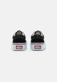Zapatillas slip-on de ante negro y lona con costuras blancas, suela de goma blanca elevada y logo rojo "Vans Off The Wall" en el talón.