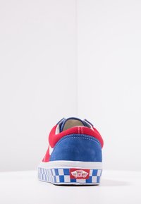 Červené a modré semišové tenisky s bílým pruhovaným bokem, kostkovaným vzorem podrážky a označenou patou. Nízký střih s polstrovaným límcem.