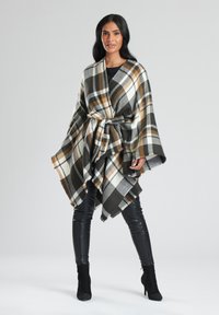 Rutigt poncho i brunt, svart och vitt, med knytmidja och vida ärmar, tillverkat i mjukt material med fransar i nederkant. Bärs över svarta byxor.