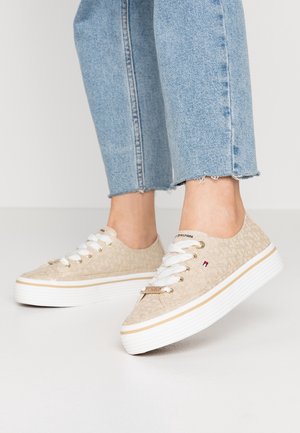 Beżowe sneakersy niskie z białymi sznurowadłami i grubymi białymi podeszwami noszone z jasnoniebieskimi, skróconymi dżinsami.