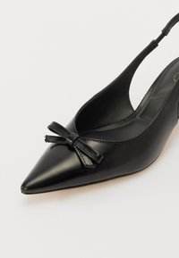 Črne usnjene slingback salonarje s konico, ki imajo poudarek z mašno na vampu in gladko, sijajno površino.